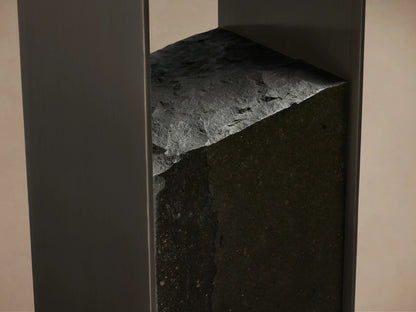 Close-up of Urben Martini Table base: dark, rough-cut marquina marble block with jagged top edge nestled between sleek dark brass supports.
