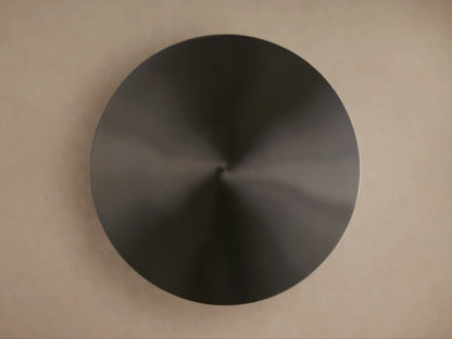 Top-down view of the Urben Martini Table's dark, circular antiqued brass tabletop with a metallic sheen on a light brown background.