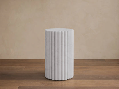 Front view of a white marble fluted cylindrical pedestal on a brown wooden floor.