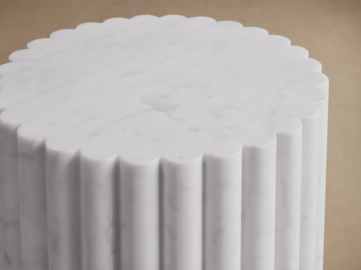Front view of a white marble fluted cylindrical pedestal on a brown wooden floor.
