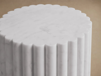 Front view of a white marble fluted cylindrical pedestal on a brown wooden floor.