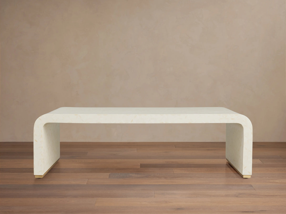 Visola Coffee Table made of ivory-colored resin and camel bone, rectangular with curved edges, on wooden floor, beige background.