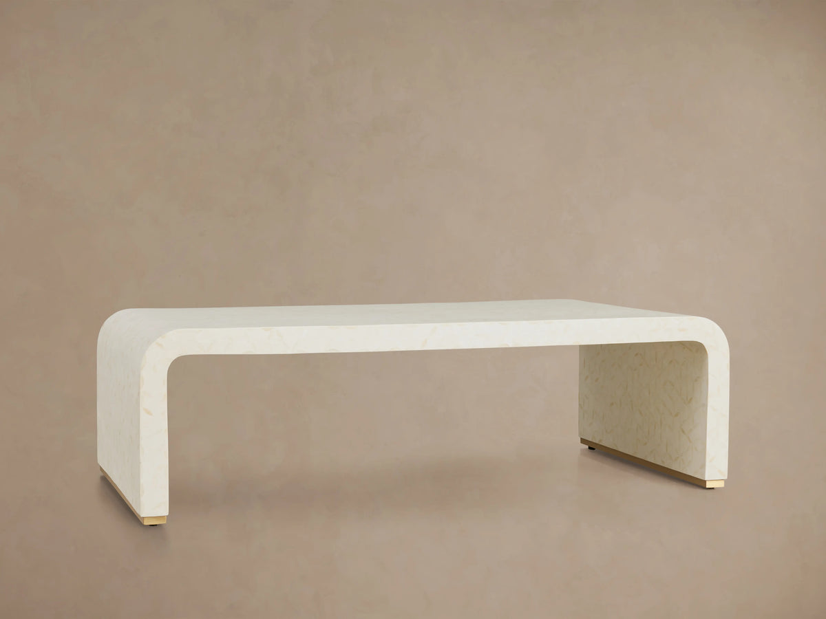 Visola Coffee Table made of ivory-colored resin and camel bone, rectangular with curved edges, on wooden floor, beige background.