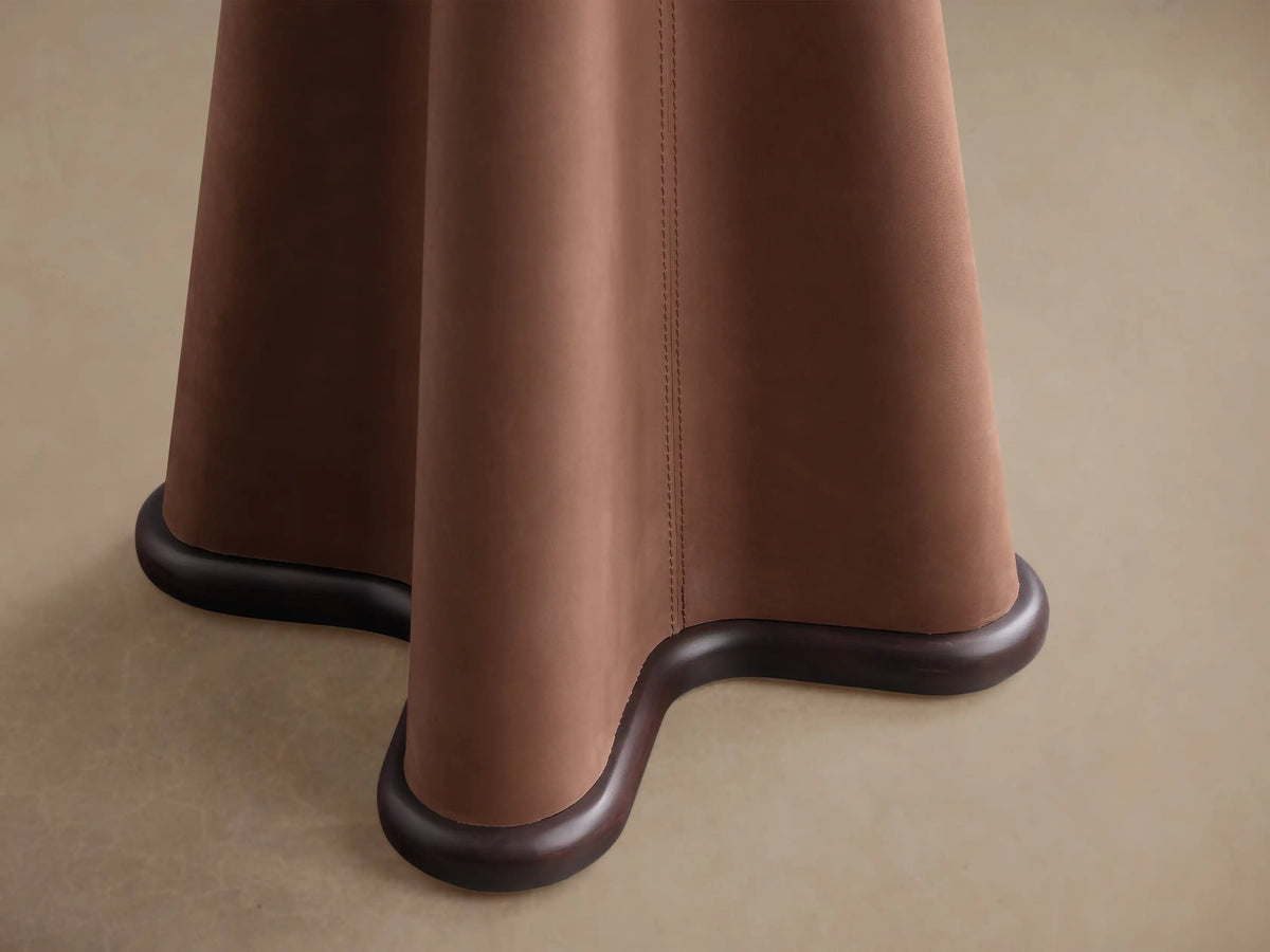 Close-up of the sculptural base of the Volant Leather End Table, featuring saddle brown leather and dark wood trim.