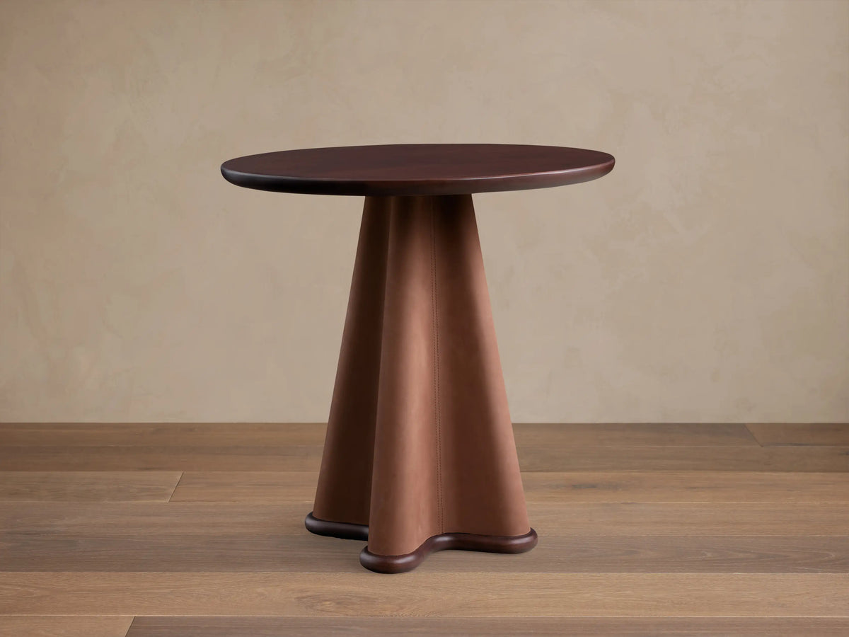 Front view of the Volant Leather End Table with a dark brown wood top and a sculptural brown leather base, featuring vertical stitching.