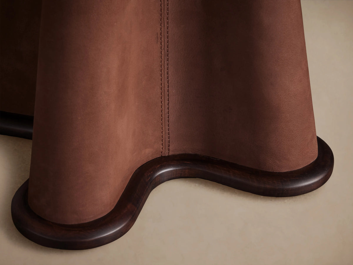 Volant Leather End Table featuring a sculptural base wrapped in brown leather with visible stitching and wood accents on a neutral background.