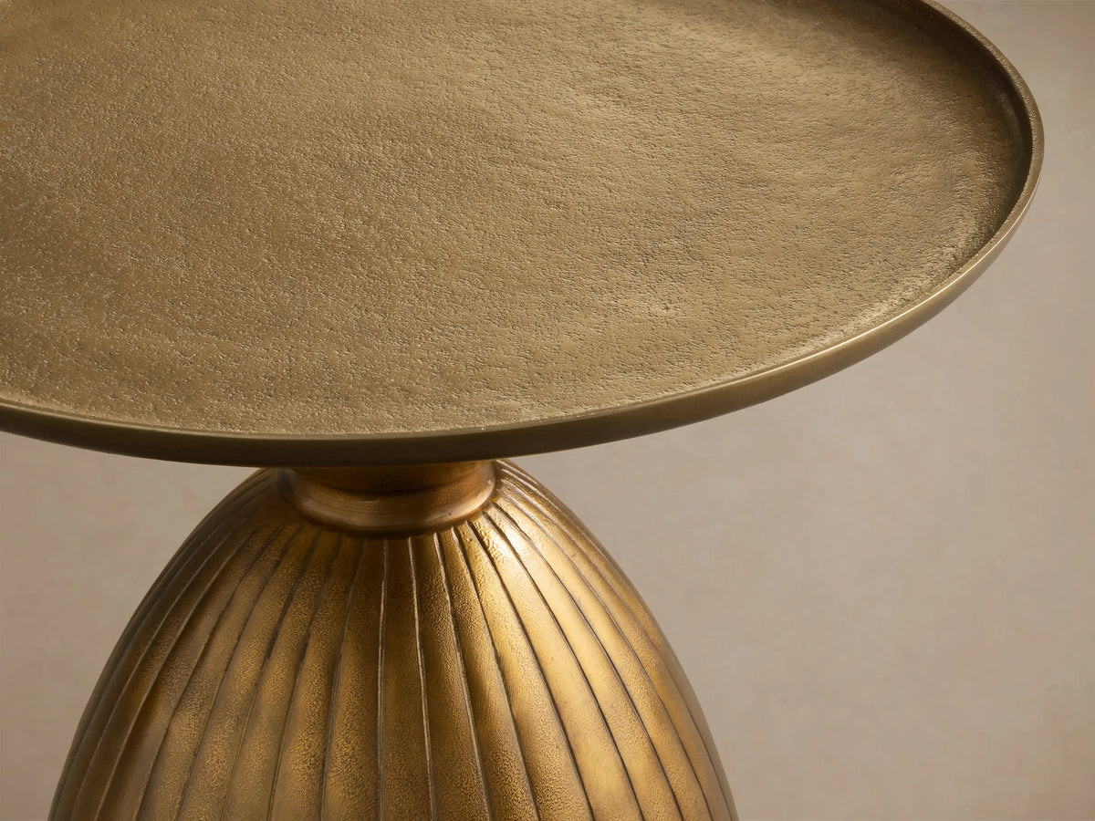 Front view of the gold Zephyr Martini Table, featuring a round top and a ribbed, curved base.