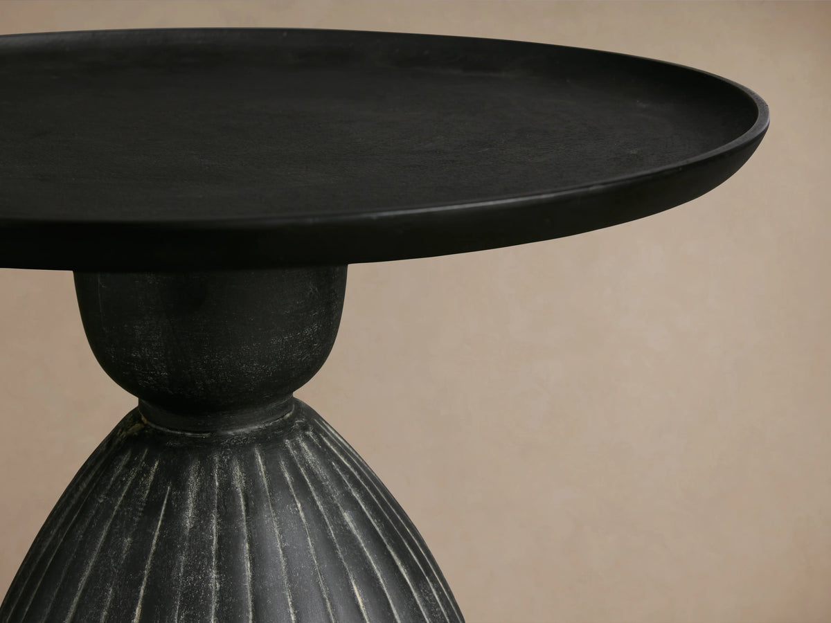 Zephyr Martini Table with a black round top and ribbed, curved, dark base featuring white glazing against a neutral background.