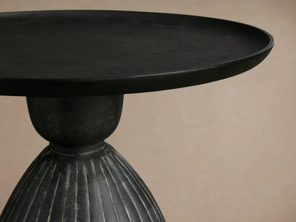 Zephyr Martini Table with a black round top and ribbed, curved, dark base featuring white glazing against a neutral background.