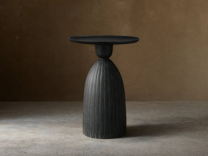 Zephyr Martini Table with black ribbed cast aluminum base and smooth round top on wooden floor, set against a beige background.