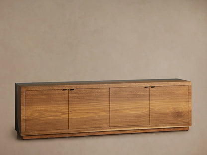 Acacius Media Console with a long, rectangular shape. Made of warm-toned wood with smooth surfaces and four cabinet doors, set against a neutral wall.