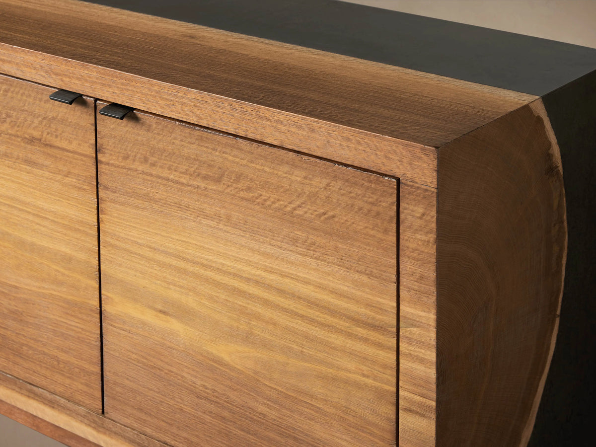 Acacius Media Console with four wooden cabinet doors, each with subtle grain patterns, set against a smooth, dark top in a neutral setting.