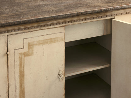 Oriana Buffet in distressed cream finish with an open door revealing two shelves and a drawer, four doors, and a flat top.