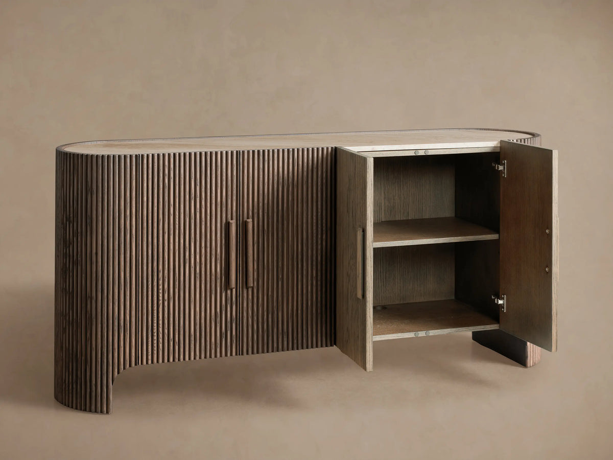 Astor Sideboard with oval marble top, dark oak reeded doors & vertical pulls, against a tan wall on a wood floor.