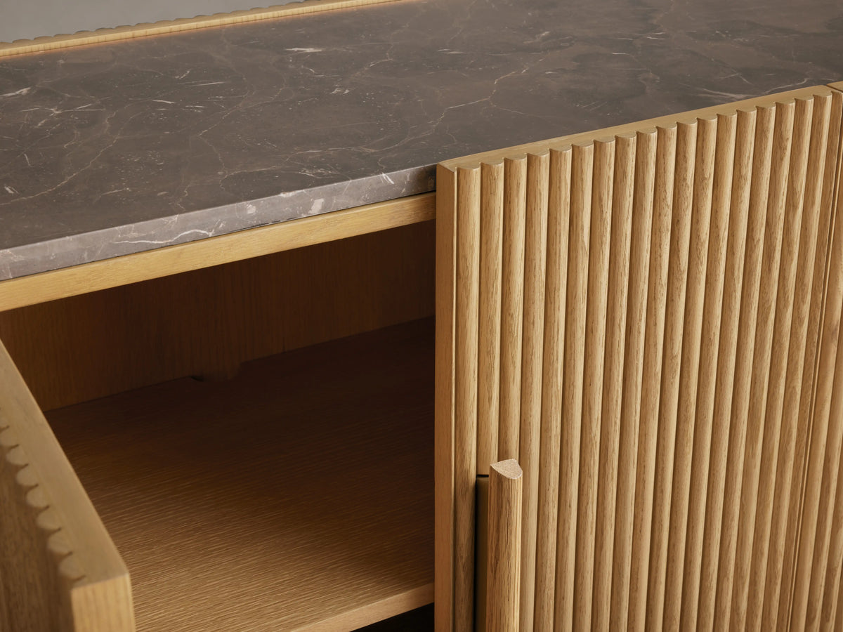 Astor Sideboard showing open wooden cabinet with reeding details, brass-accented pull, and marble stone top surface.