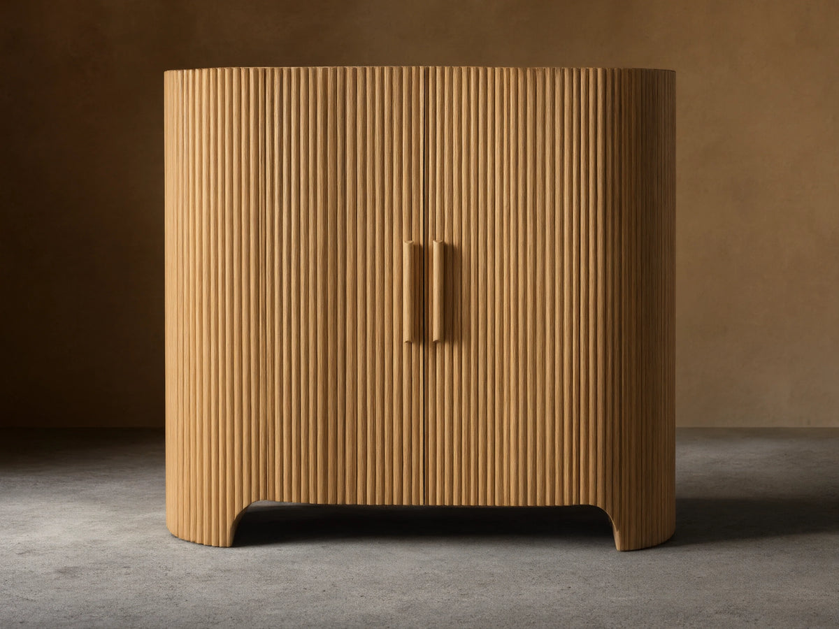 Astor Hall Chest, light oak wood cabinet with vertical reeding, rounded sides, two doors, and wooden pull handles, on wooden floor.