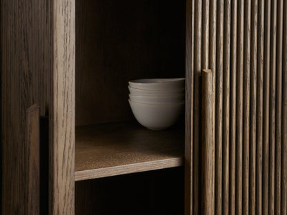 Front view of the dark brown Astor Cabinet, with a curved reeded oak veneer front and one door open to show three shelves.