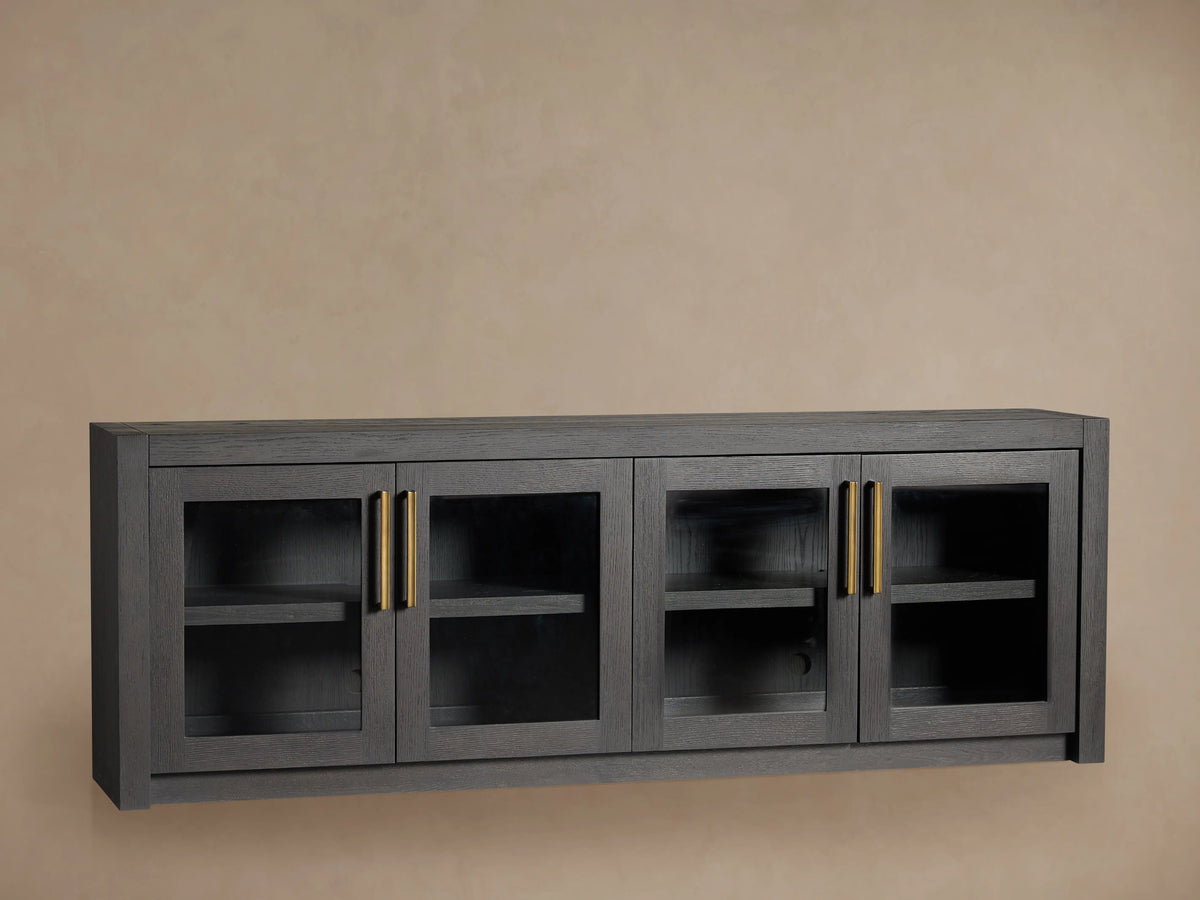 Bodhi Media Console made of dark oak with four glass-paneled doors, brass handles, and two adjustable shelves inside.
