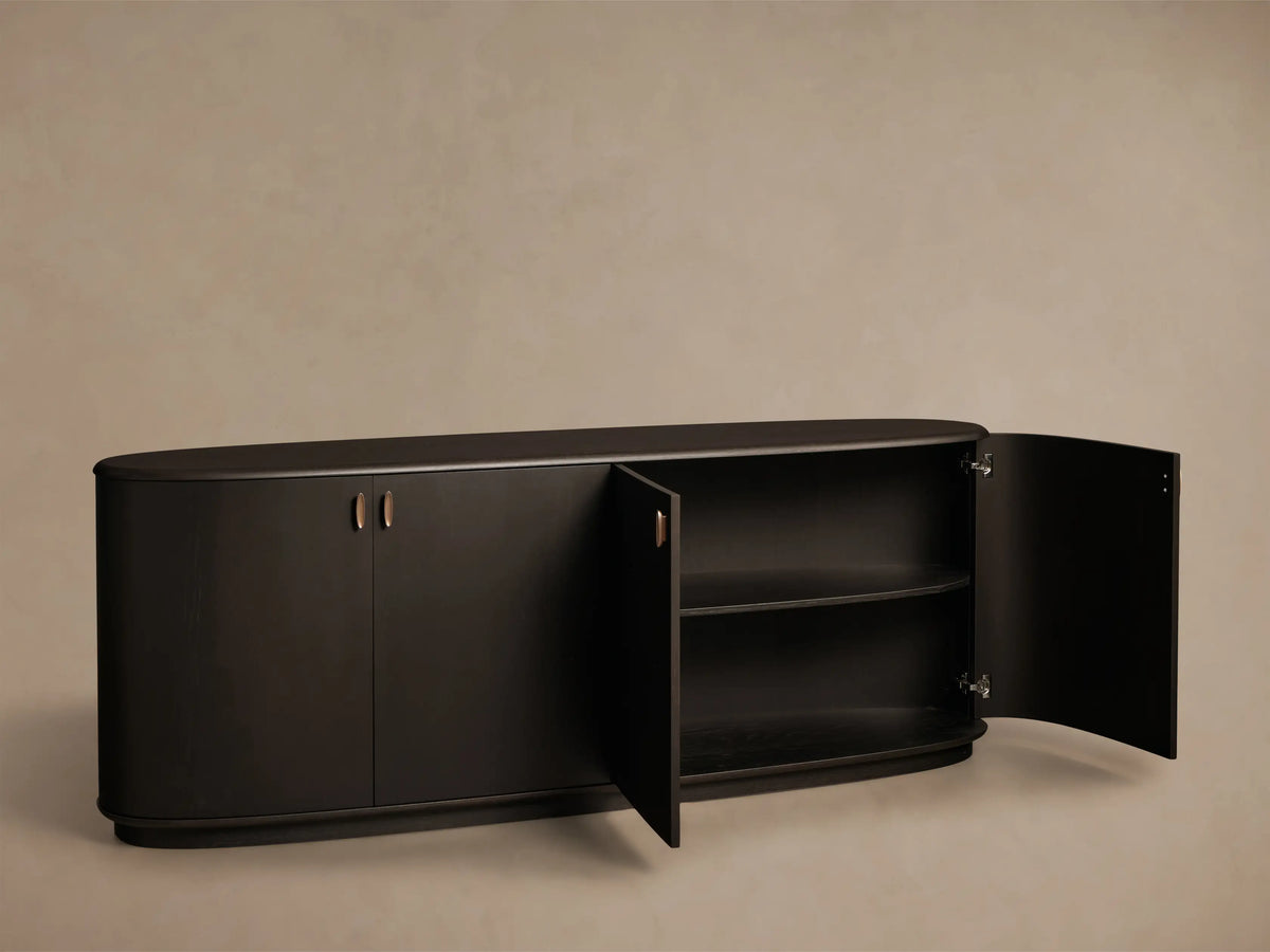 Front view of a dark brown Abanos-finished Bexler Sideboard, one curved door open showing two interior shelves, and antique bronze hardware.