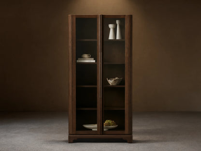 Dark wood Bardot Cabinet with two glass doors & bronze handles. Shelves hold decor items. Light wall & wood floor.