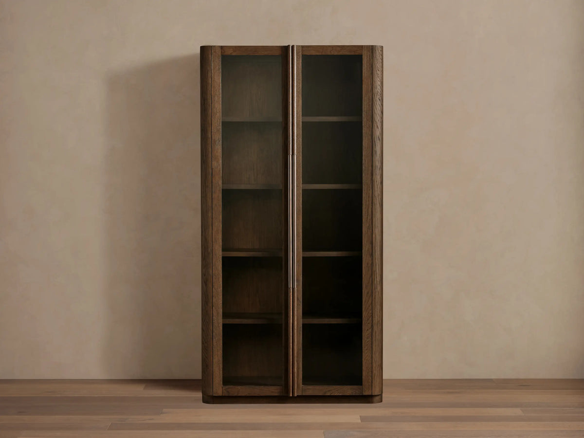 Tall, dark white oak Bardot Cabinet with two glass-paneled doors, bronze handles, and visible internal shelves.