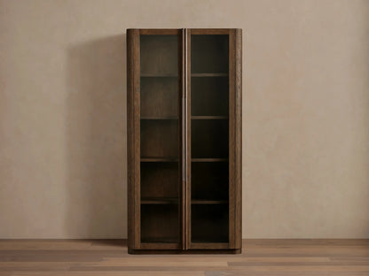 Tall, dark white oak Bardot Cabinet with two glass-paneled doors, bronze handles, and visible internal shelves.