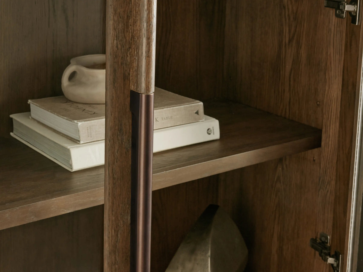 Bardot Cabinet close-up: dark stained white oak interior shelf with stacked books & light mug, bronze wood-aluminum handle.