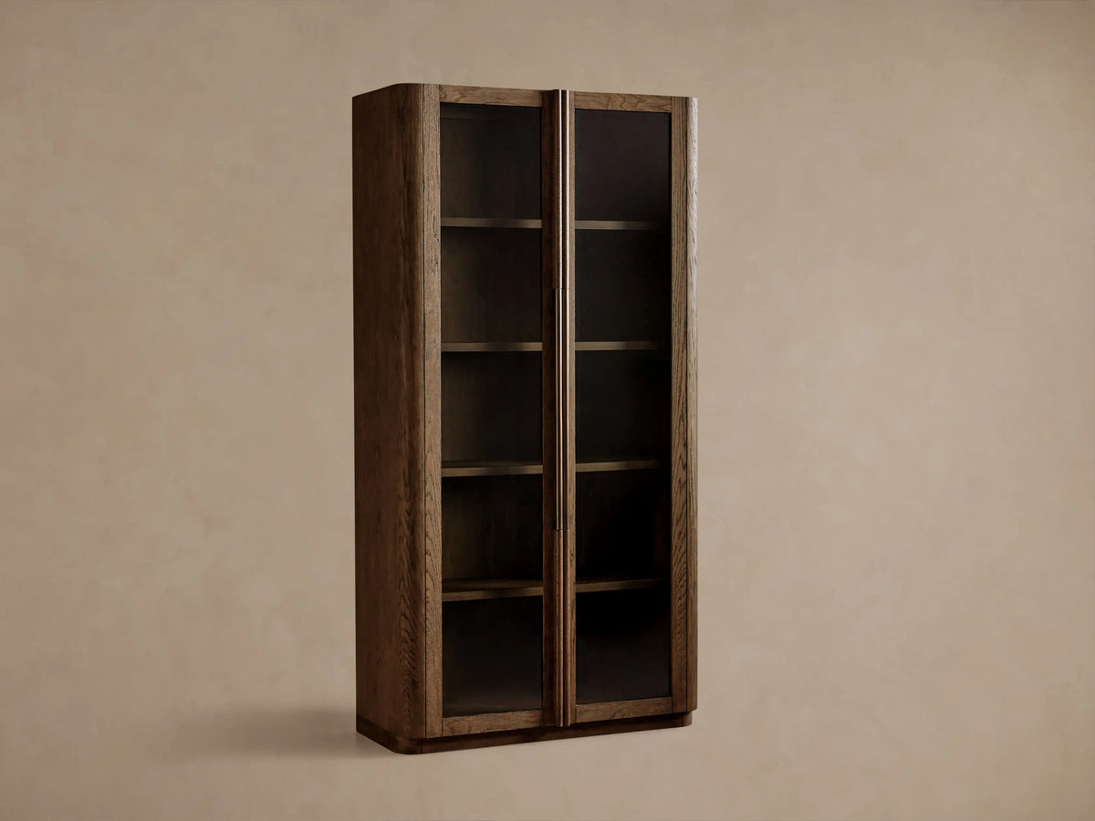 Tall Bardot Cabinet made of dark oak, with two glass-paneled doors, bronze handles, and internal shelves.