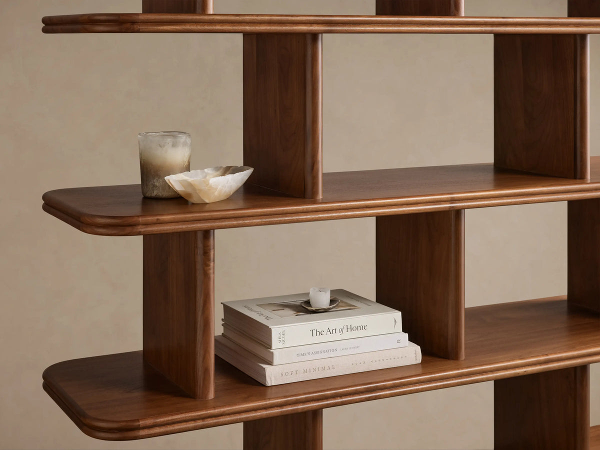 Close-up, angled view of dark brown wooden Caden Shelving with curved shelves and vertical dividers. Displays a candle, stone bowl, and books.