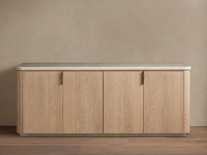Caden Sideboard in Sand finish with light wood grain, 4 doors, brushed nickel pulls, cream stone top, on wood floor.