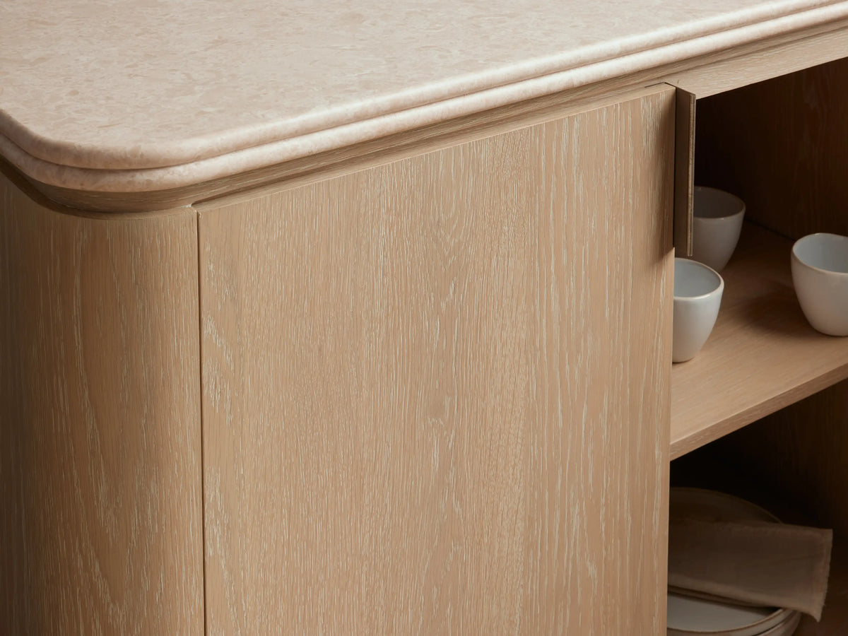 Caden Sideboard in a sand wood finish with a cream stone top, four doors, and brushed nickel handles and plinths.