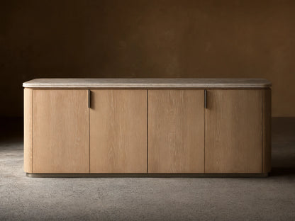 Caden Sideboard in Sand finish with light wood grain, 4 doors, brushed nickel pulls, cream stone top, on wood floor.