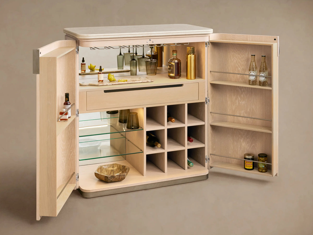 Caden Bar Cabinet: light sand oak veneer with rounded doors, cream stone top, brushed nickel pull, on a wood floor.