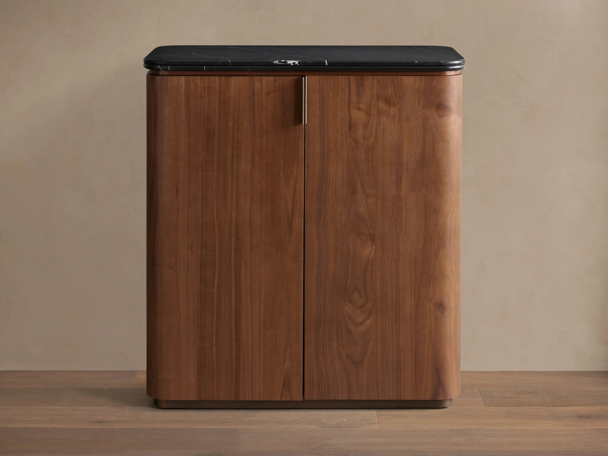Caden Bar Cabinet with walnut wood veneer, rounded front, black marble top, and subtle vertical pull.