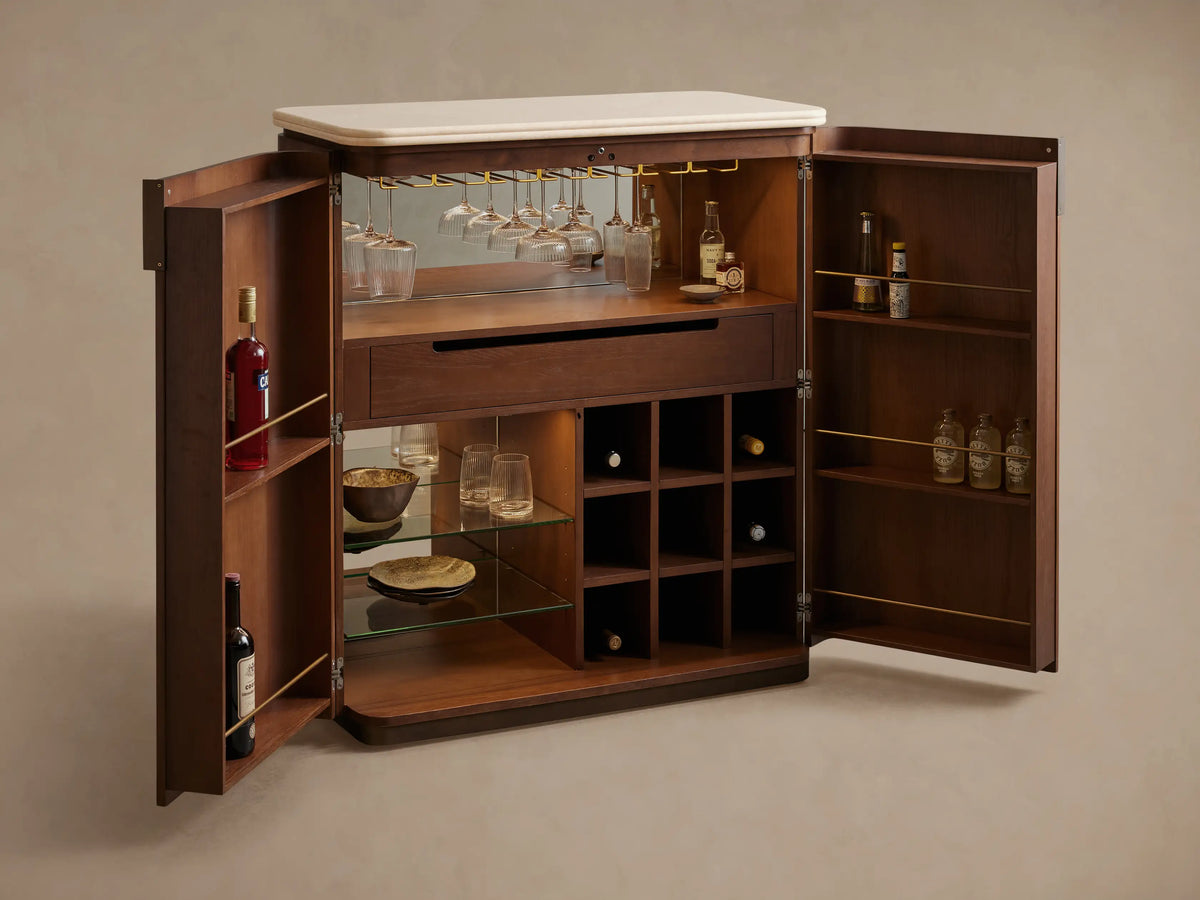 Caden Bar Cabinet in dark walnut veneer with rounded edges, cream stone top, and single bronze pull, on wood floor.