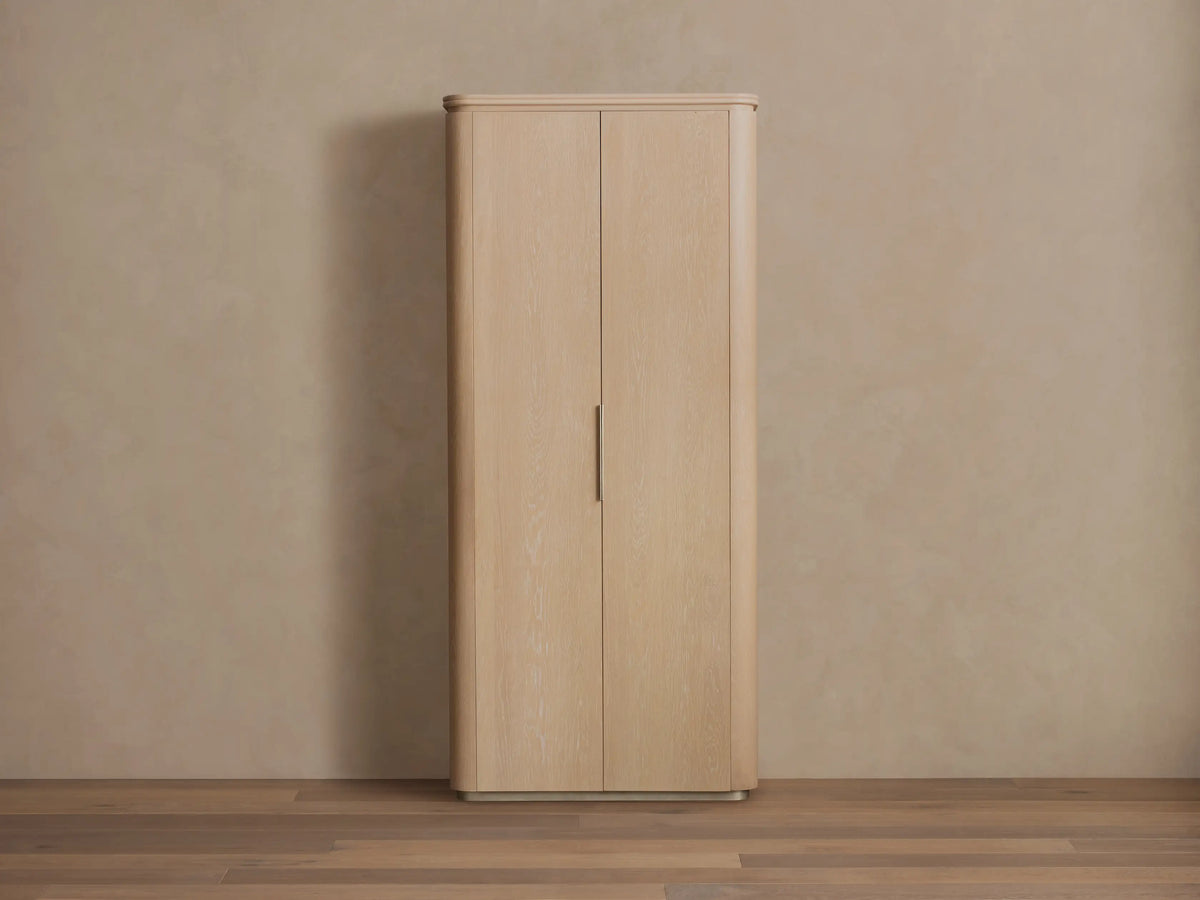 Caden Cabinet in light sand wood finish, with two rounded doors, a vertical brushed nickel handle, and plinth base.