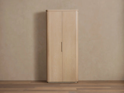 Caden Cabinet in light sand wood finish, with two rounded doors, a vertical brushed nickel handle, and plinth base.