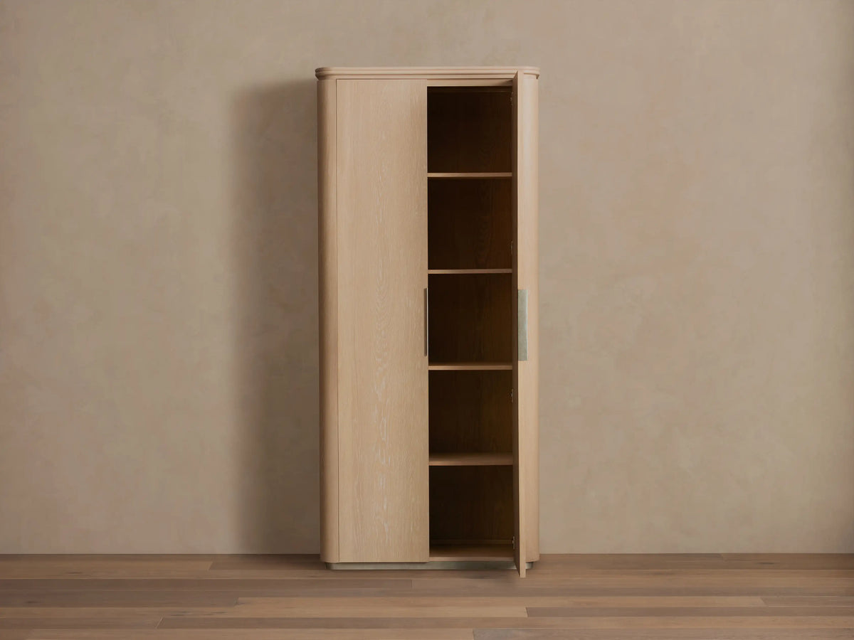 Caden Cabinet in light sand-finished American walnut wood. One door ajar, showing shelves, rounded edges & plinth base.