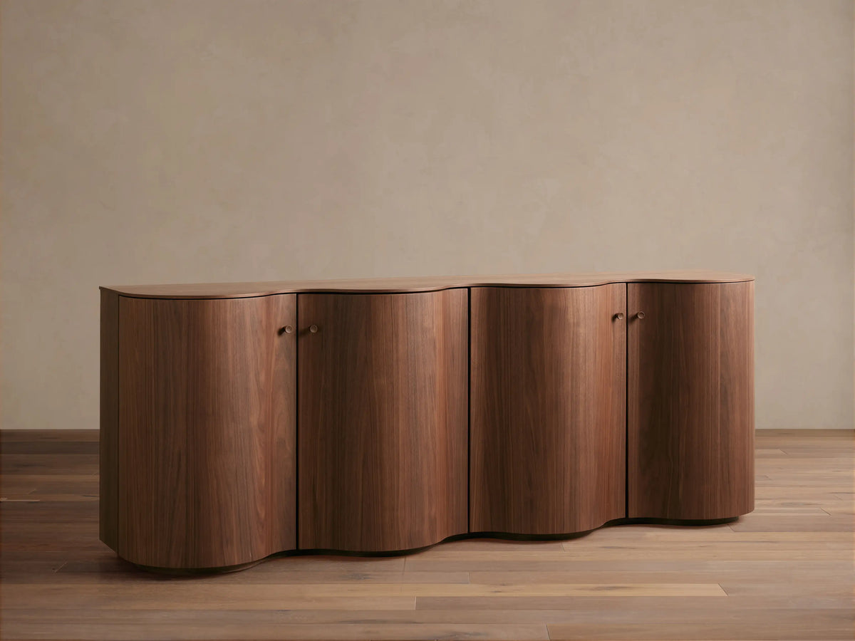 Cortina Sideboard in rich wood finish with curved edges and four cabinet doors, set against a neutral wall on wood flooring.