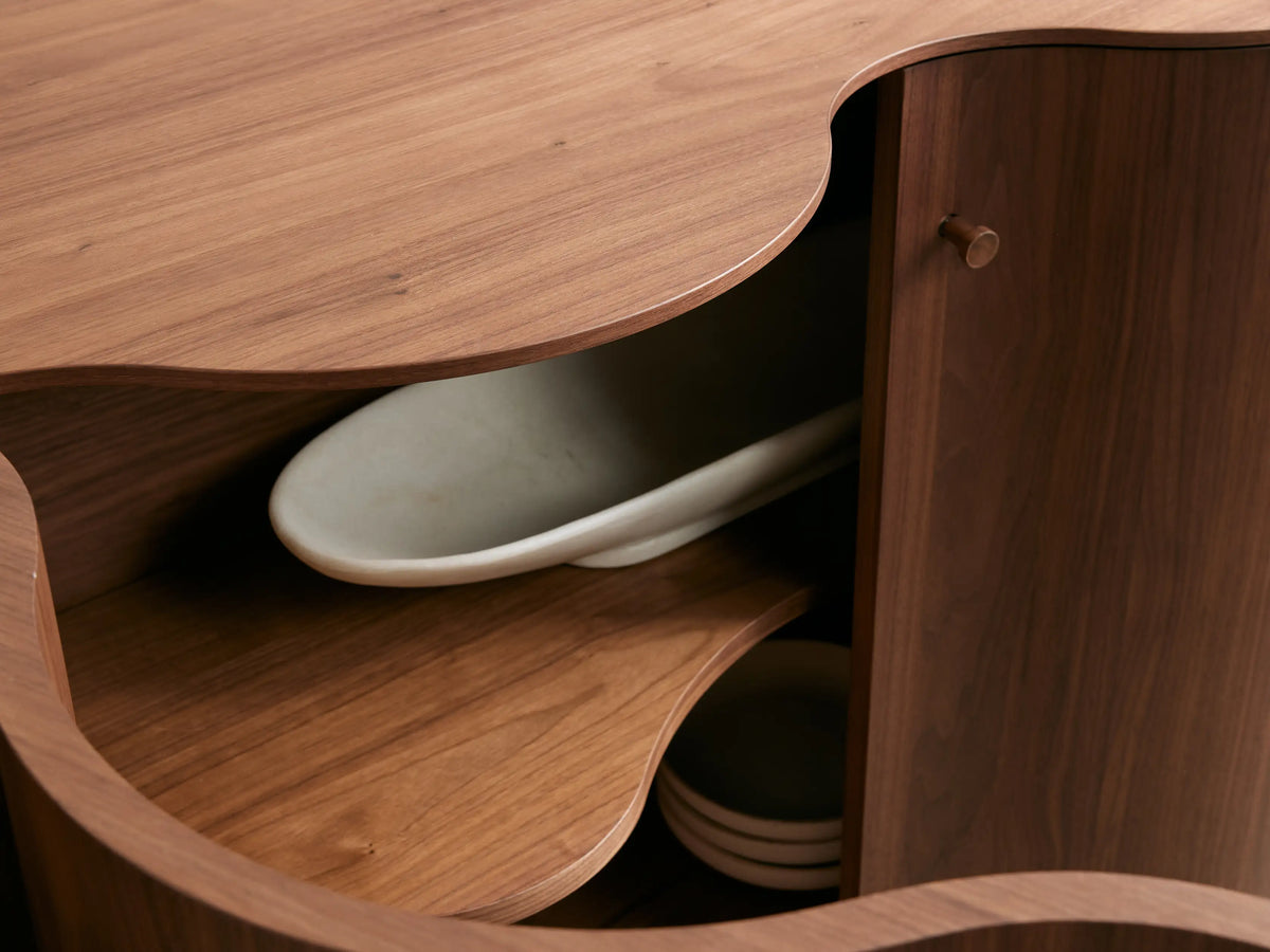 Cortina Sideboard with a wavy, contoured front design, four wooden doors, warm brown finish, and sleek metal handles.