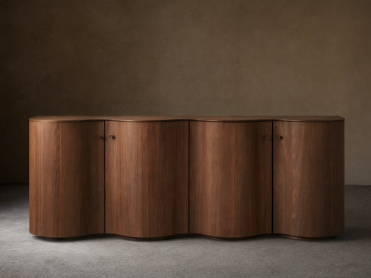 Cortina Sideboard in rich wood finish with curved edges and four cabinet doors, set against a neutral wall on wood flooring.