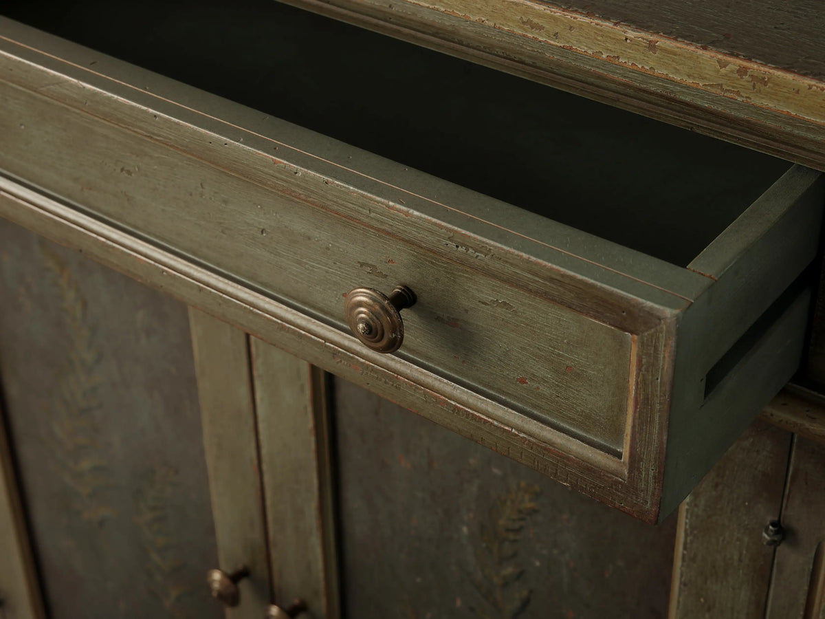 Cosetta Buffet, distressed sage green, hand-painted fern on left door, fluted facade, molded details. Right door open, shelf visible.