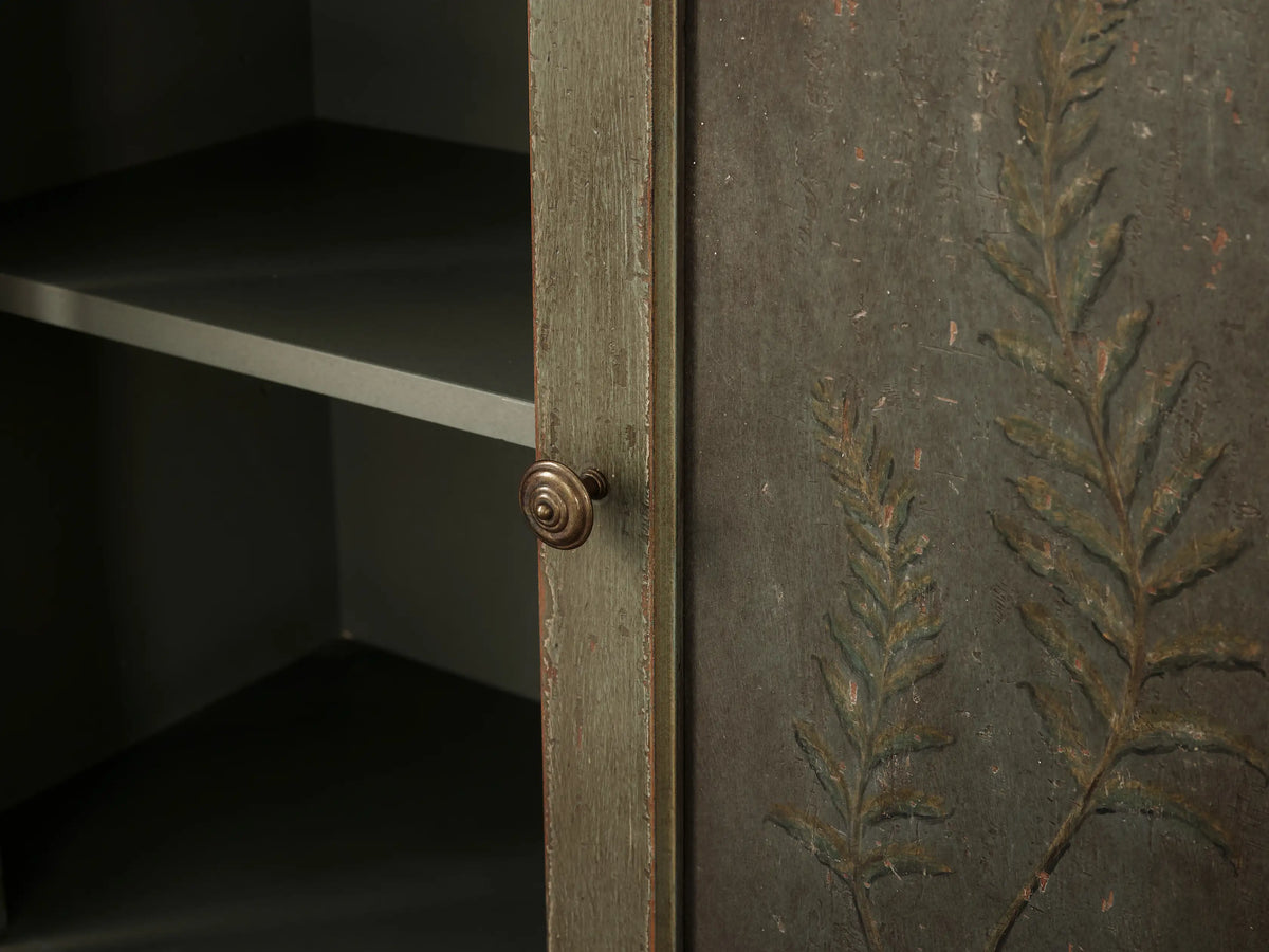Cosetta Buffet: Distressed sage green wood drawer, partially open, with an aged brass knob, above cabinet doors with faint decor.