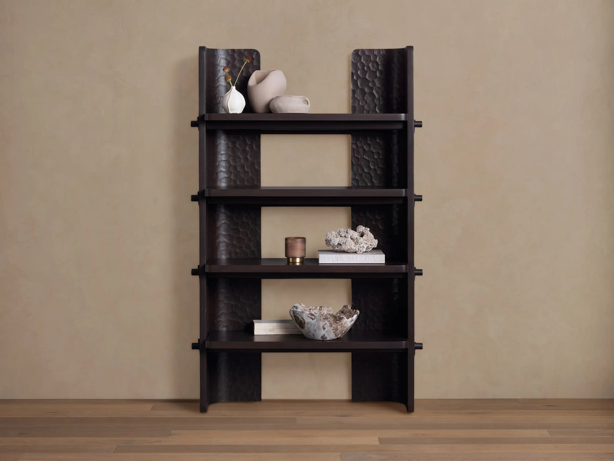 Dark brown chiseled bookcase made of handcrafted mahogany wood with four open shelves, standing against a beige wall.