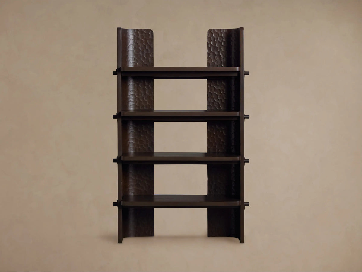 Dark brown chiseled bookcase made of handcrafted mahogany wood with four open shelves, standing against a beige wall.