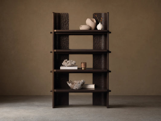 Dark brown chiseled bookcase made of handcrafted mahogany wood with four open shelves, standing against a beige wall.