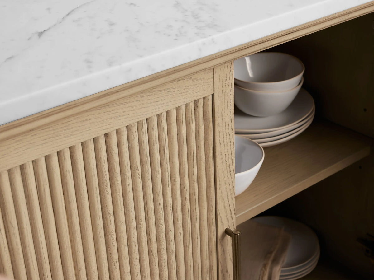 Coventry Buffet: Light oak wood cabinet with fluted doors, white Carrara marble top. Right door open, revealing interior shelf. Antique brass handle.