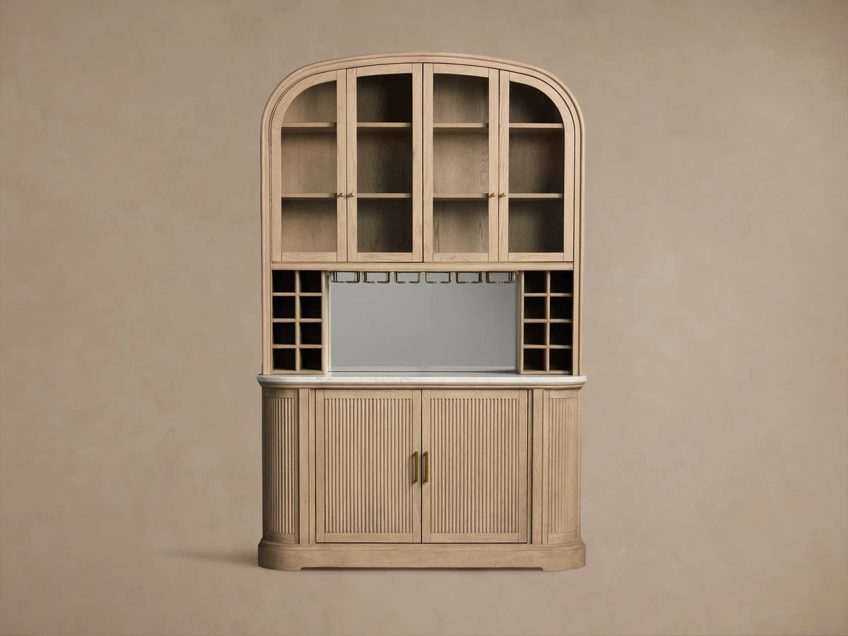 Light oak Coventry Bar with arched glass top cabinets, mirrored middle section with wine racks, white marble counter, and fluted wood base.