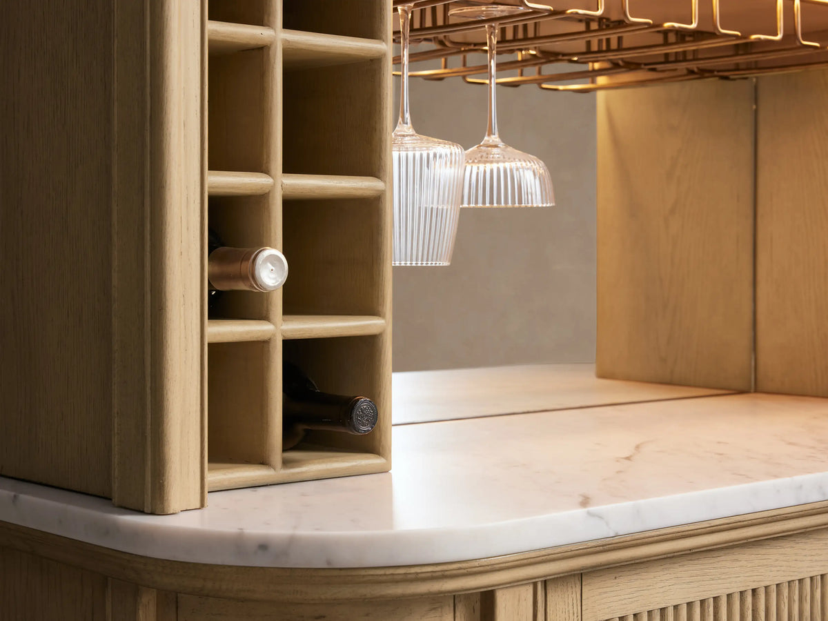 Coventry Bar: light oak wine rack with bottles, white Carrara marble top, antique brass stemware holder, two clear fluted glasses.