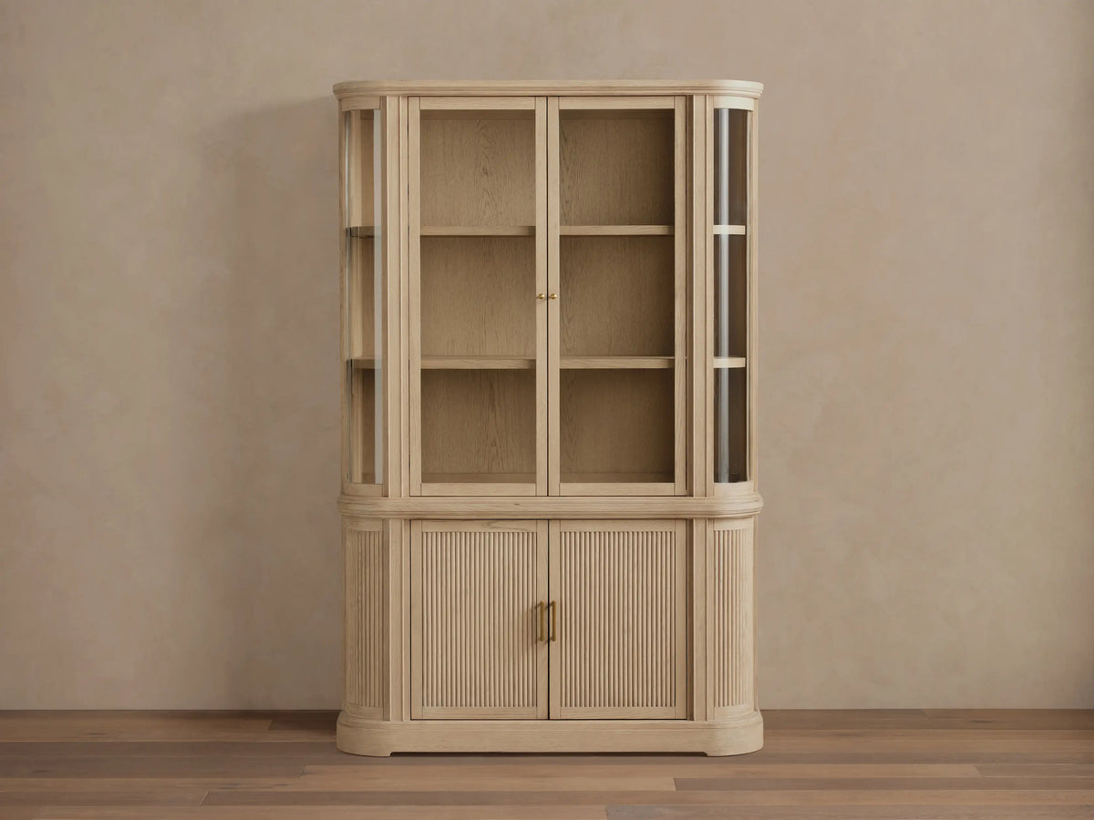 Coventry Cabinet: Light white oak display cabinet with glass top doors & illuminated shelves, one fluted bottom door ajar.